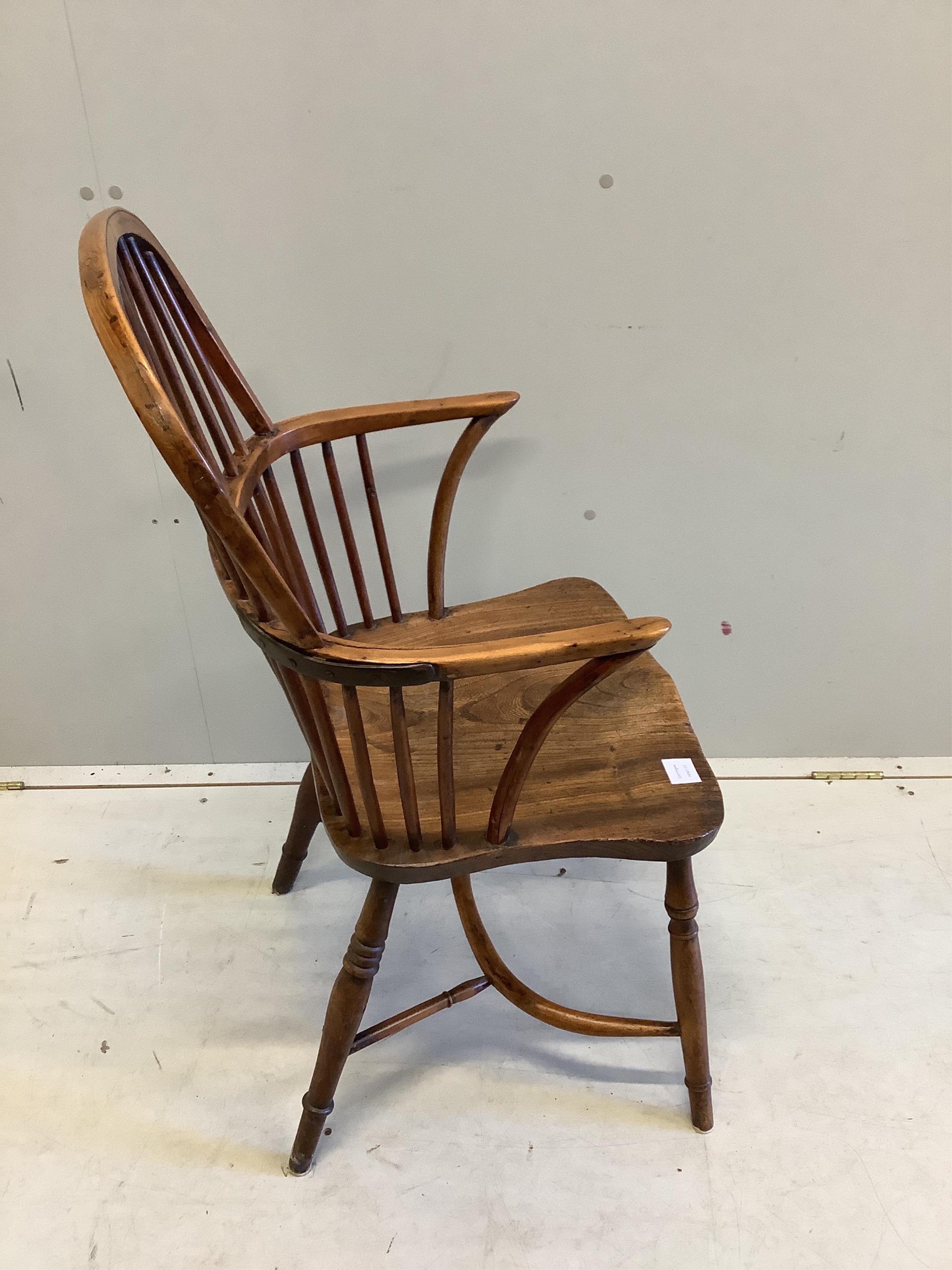 An early 19th century yew and elm comb back Windsor elbow chair with crinoline stretcher, width 53cm, depth 42cm, height 99cm. Condition fair, arm rail split to left side, left leg now misshapen with minor chips.